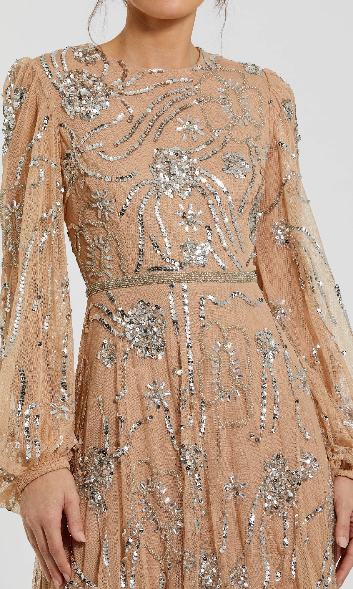 A woman in the Mac Duggal 9472 Long Sleeve Sequin Formal Dress, a sheer nude gown embellished with silver sequin and beaded floral and abstract designs.